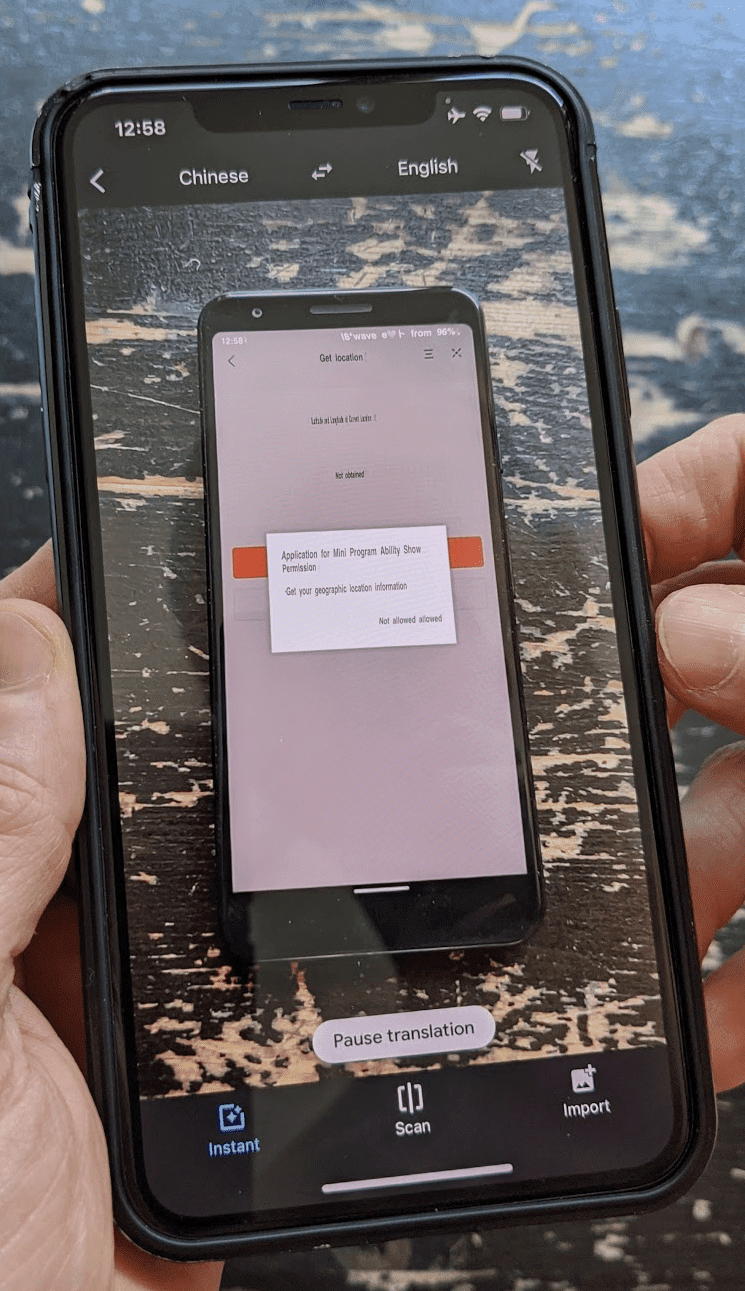 Drugi telefon z Tłumaczem Google w trybie aparatu tłumaczący na żywo interfejs chińskiej miniaplikacji uruchomionej na telefonie głównym.